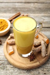 Delicious turmeric latte in glass cup, roots and spices on wooden table, closeup