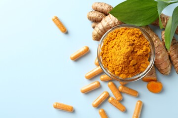 Turmeric capsules, powder, roots and green leaves on light blue background, flat lay. Space for text