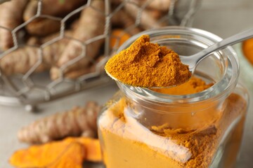 Taking aromatic turmeric powder with spoon from glass jar at table, closeup