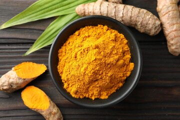 Aromatic turmeric powder in bowl, fresh roots and leaves on wooden table, flat lay