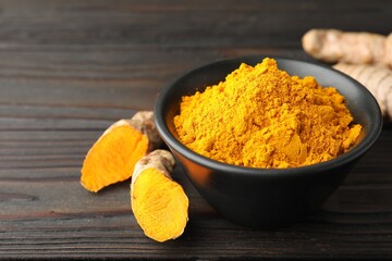 Aromatic turmeric powder in bowl and fresh roots on wooden table, closeup. Space for text