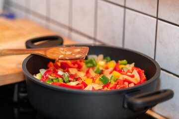 A cooking pot on gas fire. fresh cut paprikas in a cooking pot on gas stove. The gas fire is on. Healthy food cooking, home made healthy dinner. Fresh vegetables. A wooden spoon on the edge of the pot