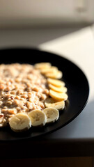 Oatmeal with banana slices on a black plate in natural sunlight