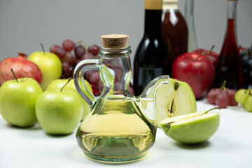 Apple cider vinegar in a vinegar cruet with spout on the background of other types of vinegars and fruits.