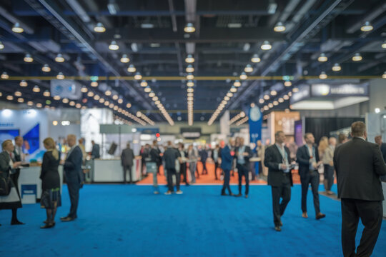 Large exhibition hall blue carpeted floor high ceiling Abstract blur people
