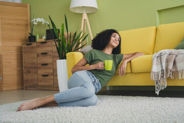 Full size photo of pretty young woman sit floor hold coffee contemplate pastime living room...