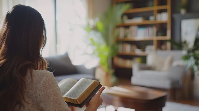 A young woman in a quiet, cozy room reads the Bible.