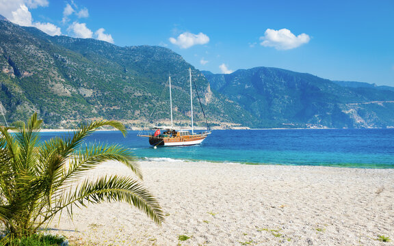 Oludeniz beach with blue sea, anchored sightseeing boat, majestic mountains and blue sky on Mediterranean coast of Turkey. Welcome to Oludeniz - turkish riviera - Powered by Adobe