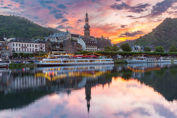 Fototapeta premium Evening view of Cochem, with illuminated boats on the Moselle River reflecting the colorful sunset sky, Germany