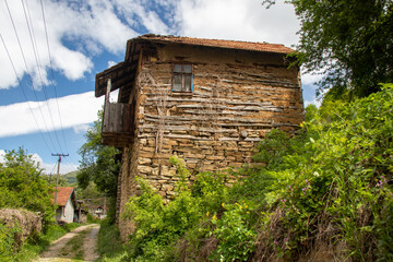 Historic stone house stands on a serene countryside road under a bright blue sky in a rural area