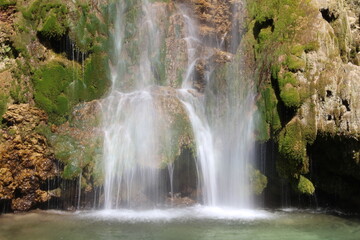 Majestic waterfall cascading over rocky cliffs in a lush green landscape during bright daylight