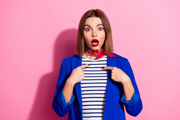 Surprised young woman gesturing by pointing at herself against a vibrant pink background,...
