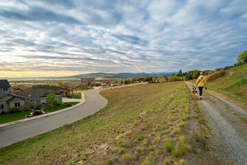 A woman with a hat walks her dog on a paved hillside walking trail in a luxury community of view...