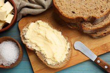 Fresh bread with butter, salt and knife on blue wooden table, flat lay