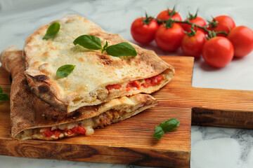 Halves of tasty calzone with meat, cheese, basil and tomato on white marble table, closeup