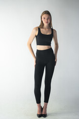professional model in a sleek black outfit adjusts her jeans while gazing off-camera, showcasing...