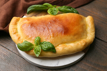 Tasty vegetarian calzone with basil on wooden table, closeup