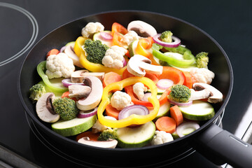 Frying pan with mix of vegetables and mushrooms on cooktop, closeup