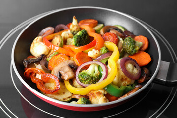Frying pan with mix of vegetables and mushrooms on cooktop, closeup