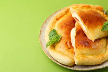 Pieces of delicious calzone pizza with mozzarella, tomatoes and basil on green background, closeup. Space for text