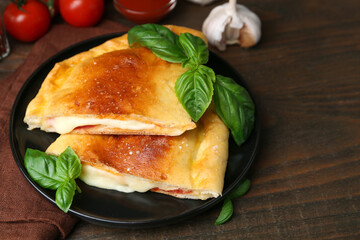 Pieces of delicious calzone pizza with mozzarella, tomatoes and basil on wooden table, closeup