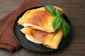 Pieces of delicious calzone pizza with mozzarella, tomatoes and basil on wooden table, closeup