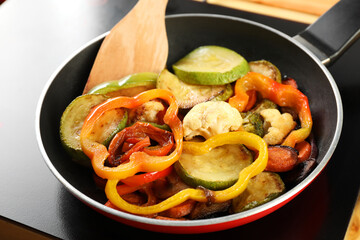 Frying pan with vegetables and stove on table, closeup