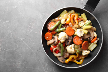 Different vegetables and mushrooms in frying pan on grey table, top view. Space for text