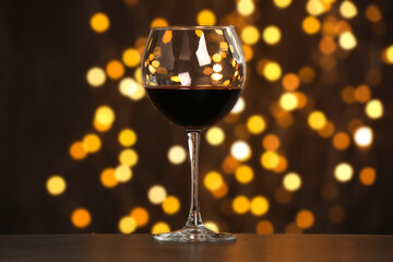 Tasty red wine in glass on table against dark background with blurred lights, bokeh effect