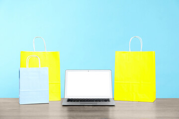 Internet shopping. Laptop and colorful paper bags on wooden table against light blue background
