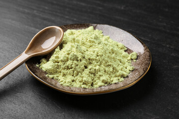 Plate with dry wasabi powder and spoon on dark textured table, closeup