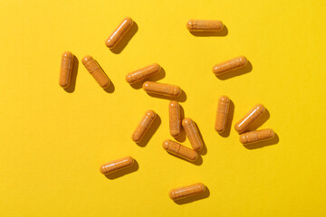 Many turmeric capsules on yellow background, flat lay