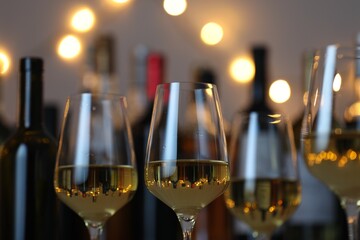 Tasty white wine in glasses against blurred background with festive lights, closeup. Bokeh effect