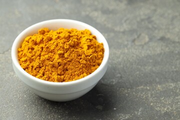 Turmeric powder in bowl on grey table, closeup. Space for text