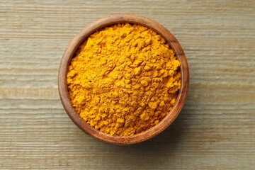 Turmeric powder in bowl on wooden table, top view