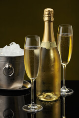 Bottle of sparkling wine, glasses and cooler bucket on black mirror surface