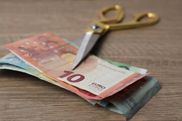 Euro banknotes and scissors on wooden table, closeup