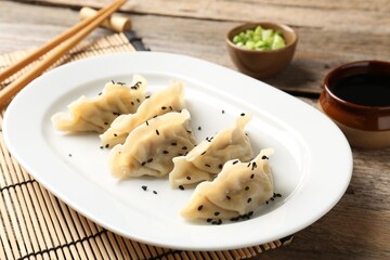 Delicious gyoza dumplings with sesame seeds served on wooden table, closeup