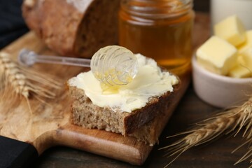 Tasty sandwich with butter, honey and dipper on wooden table, closeup