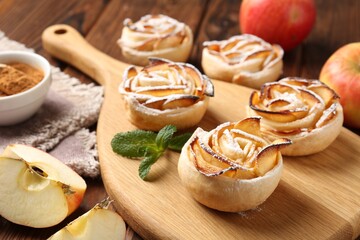 Tasty apple roses with powdered sugar served on wooden table, closeup