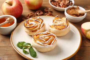 Tasty apple roses with powdered sugar served on wooden table, closeup