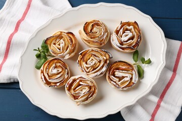 Tasty apple roses with powdered sugar served on blue wooden table, top view