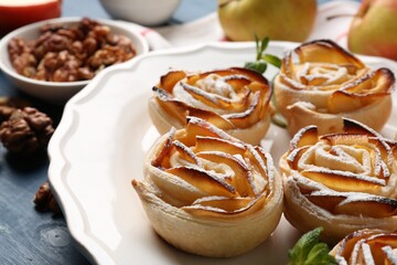 Tasty apple roses with powdered sugar served on blue wooden table, closeup