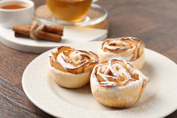 Freshly baked apple roses, honey, cinnamon sticks and tea on wooden table, closeup