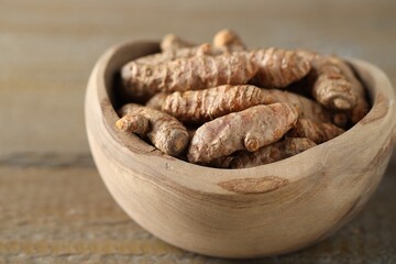Raw turmeric roots in bowl on wooden table, closeup