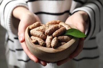 Woman holding bowl with raw turmeric roots, closeup