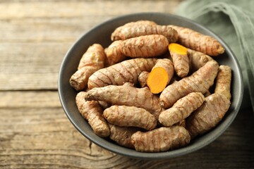 Tumeric rhizomes in bowl on wooden table, closeup