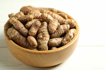 Tumeric rhizomes in bowl on white wooden table, closeup