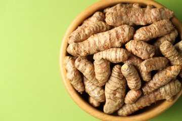 Tumeric rhizomes in bowl on green background, top view