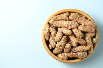 Tumeric rhizomes in bowl on light blue background, top view. Space for text